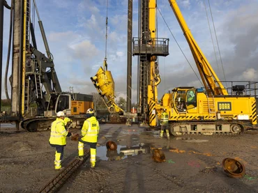 Bild zeigt eine Ramme. Davor steht ein Bauarbeiter.